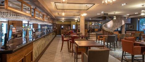 A restaurant with a bar area, seating, and a staircase.