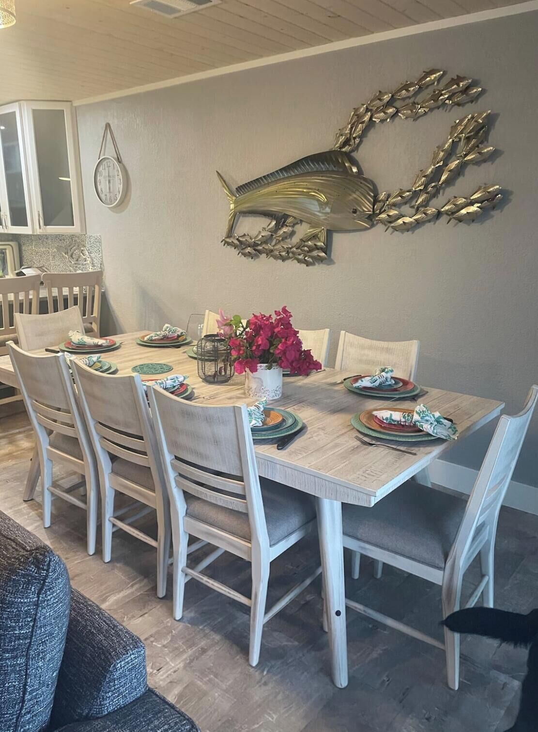 Comedor con una mesa de madera dispuesta para cuatro personas, rodeado de sillas blancas.