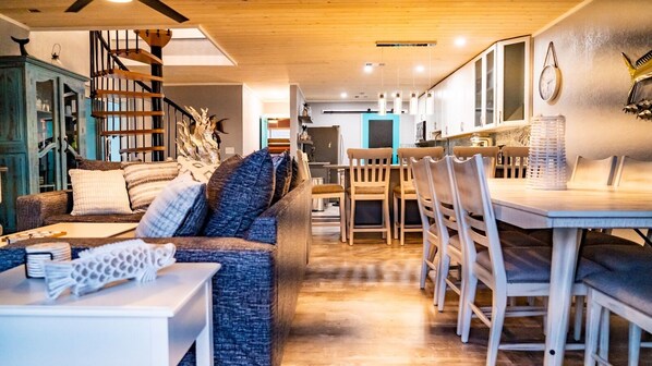 Un salon moderne avec un canapé, une table à manger et des chaises. Un escalier mène à l’étage supérieur.