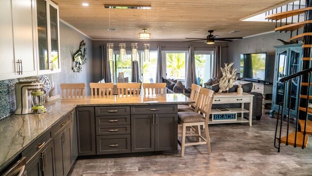 A kitchen with a central island, wooden chairs, a dining table, and a staircase.