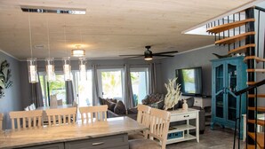 A spacious living area with a dining table, chairs, a sofa, a TV, and a staircase.