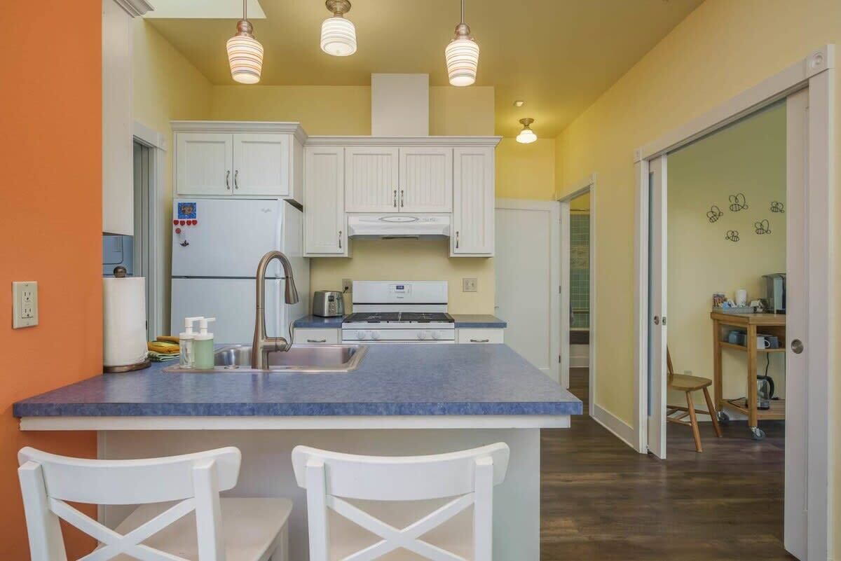 A kitchen with white cabinets, a blue countertop, and a central island with two white chairs.