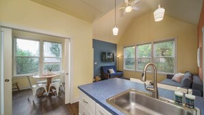 A kitchen with a blue countertop, a sink, and a dining area with white chairs. - #StayInMyDistrict Lake Oswego Honey Bee Cottage (Lake Oswego)