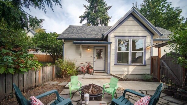 A house with a patio area featuring two green chairs and a table, a fire pit, and a bicycle parked outside. - #StayInMyDistrict Lake Oswego Honey Bee Cottage (Lake Oswego)