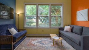 A living room with a blue sofa, a grey sofa, a wooden coffee table, and a patterned rug. - #StayInMyDistrict Lake Oswego Honey Bee Cottage (Lake Oswego)