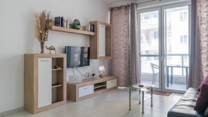 Een moderne woonkamer met een flatscreen televisie, houten kasten, een kleintje tafeltje en een bank.