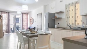Een moderne keuken met witte kasten, een roestvrijstalen koelkast en een eethoek met een tafel voor vier personen.