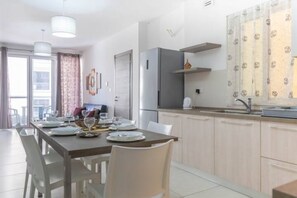 A modern kitchen with a dining area, featuring a stainless steel refrigerator, white cabinets, and a dining table set for four.
