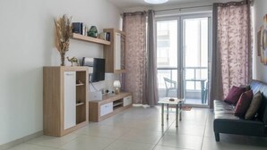 Een moderne woonkamer met een televisie, een houten kast, een bank en een eethoek met een tafel en stoelen.