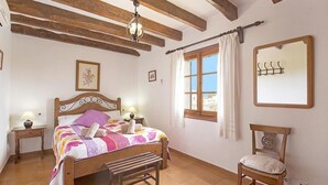 A bedroom with a wooden bed, a bench, a chair, a window with curtains, a mirror, and a chandelier. - Finca Can Tomeu, private pool, wifi, 4 bedrooms, 10 minutes to the beach  (Pollenca)