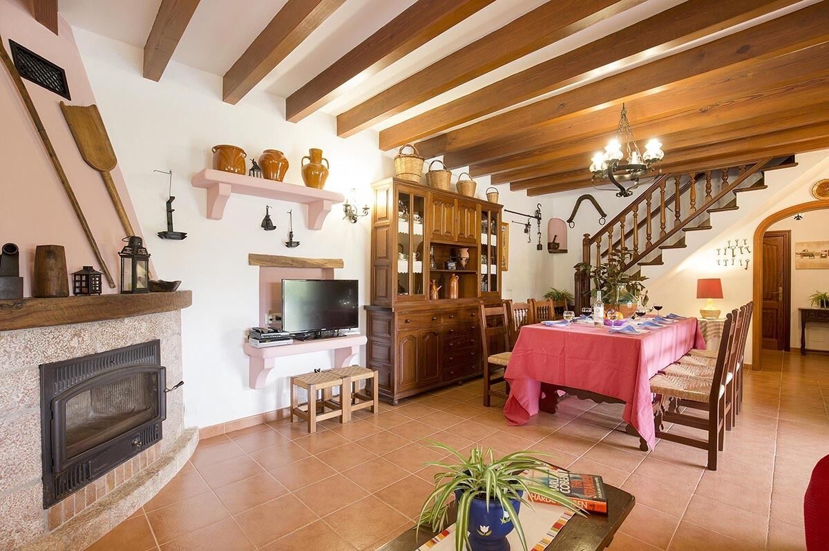 Una sala de estar acogedora con chimenea, vigas de madera, un comedor con mantel rojo y una escalera que sube.