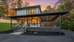 Ein modernes, zweistöckiges Haus mit einer überdachten Veranda, einer Treppe zum Eingang und einem gepflegten Rasen.
