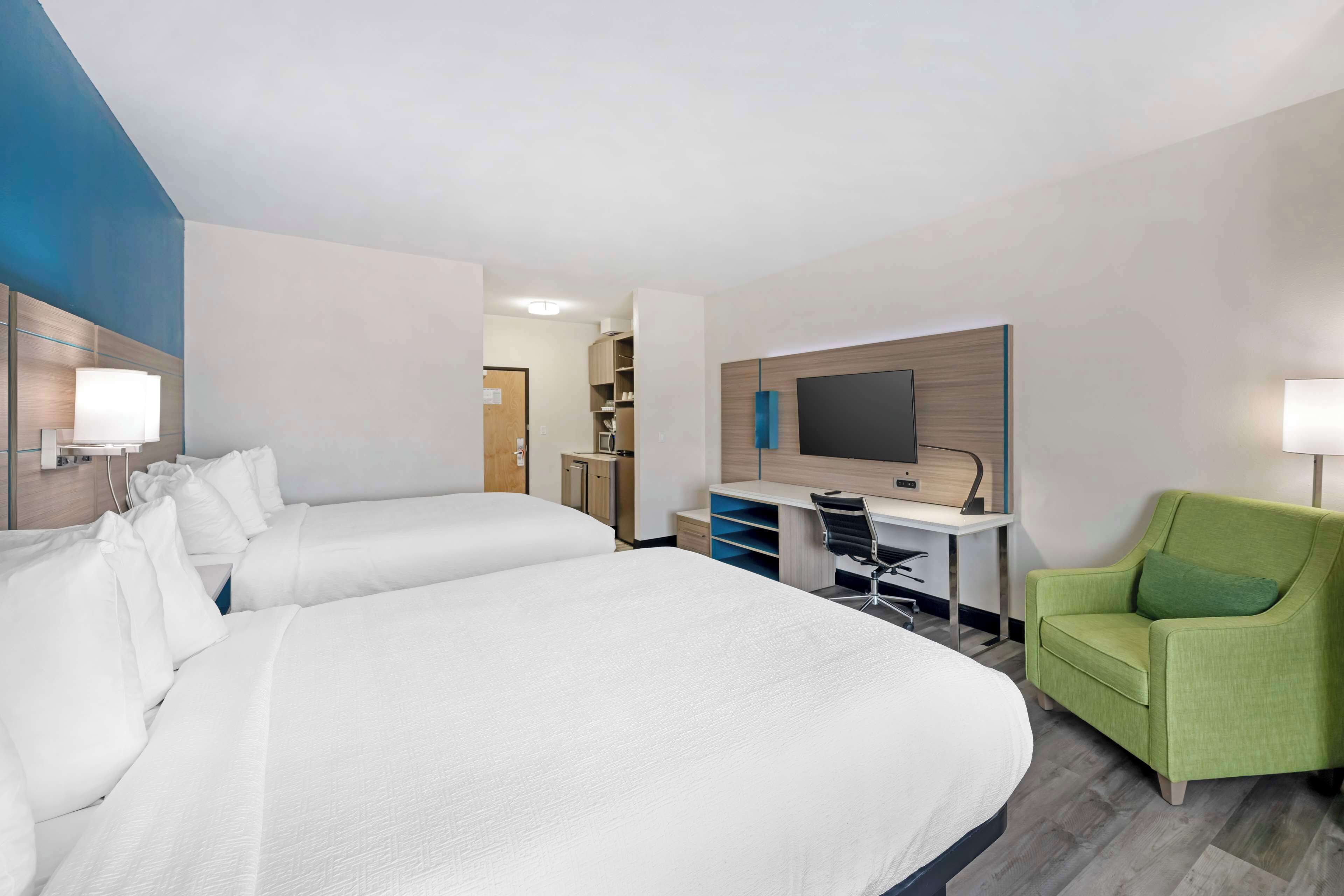A hotel room with two beds, a desk, a chair, a TV, and a bathroom visible in the background.