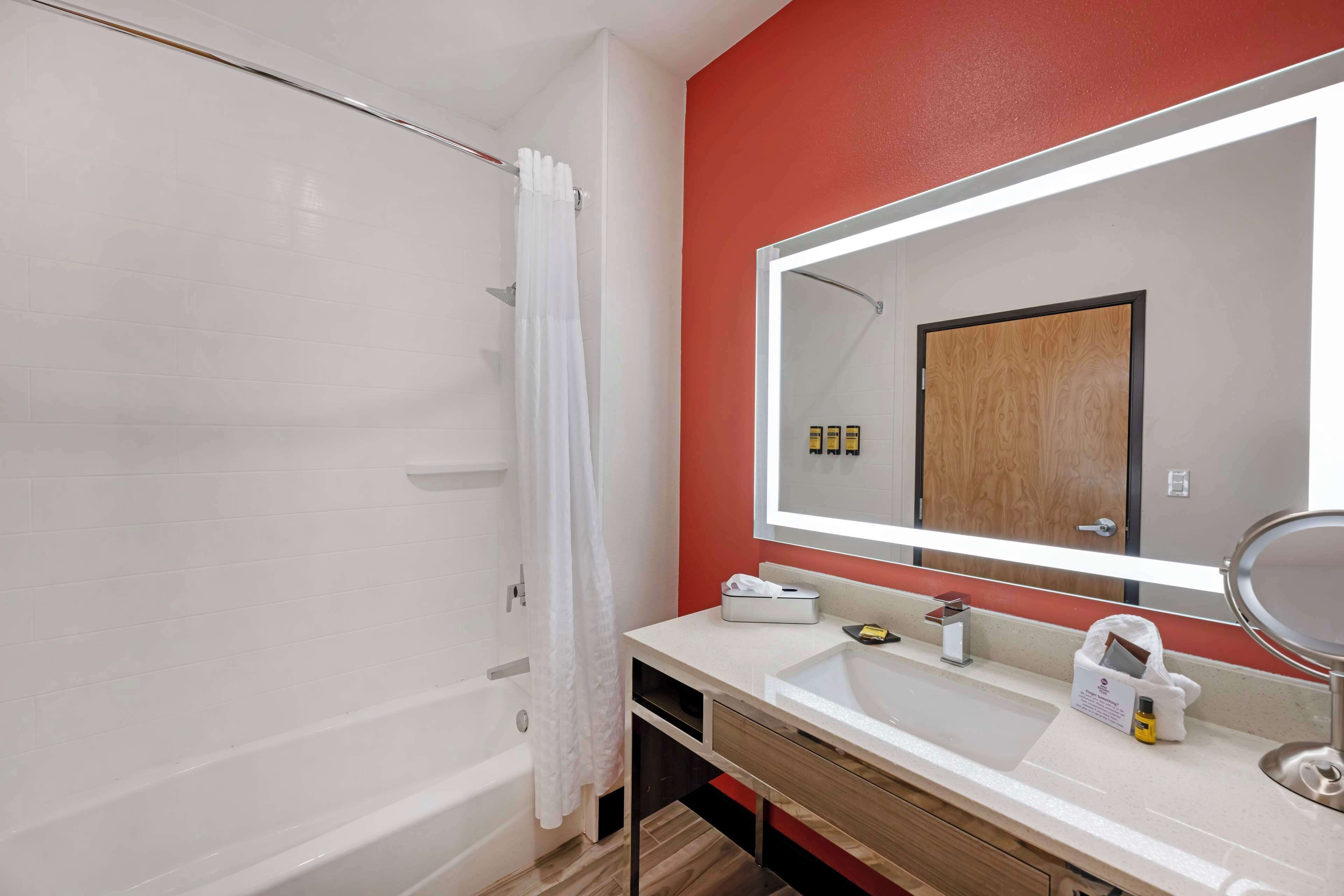 A modern bathroom with a white bathtub, a large mirror, a vanity with a sink, and a shower area.