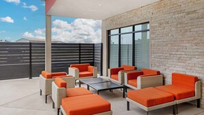 A modern outdoor seating area with wicker furniture and orange cushions, a glass wall, and a view of the sky. - Best Western Plus Executive Residency Carlsbad Hotel (Carlsbad)