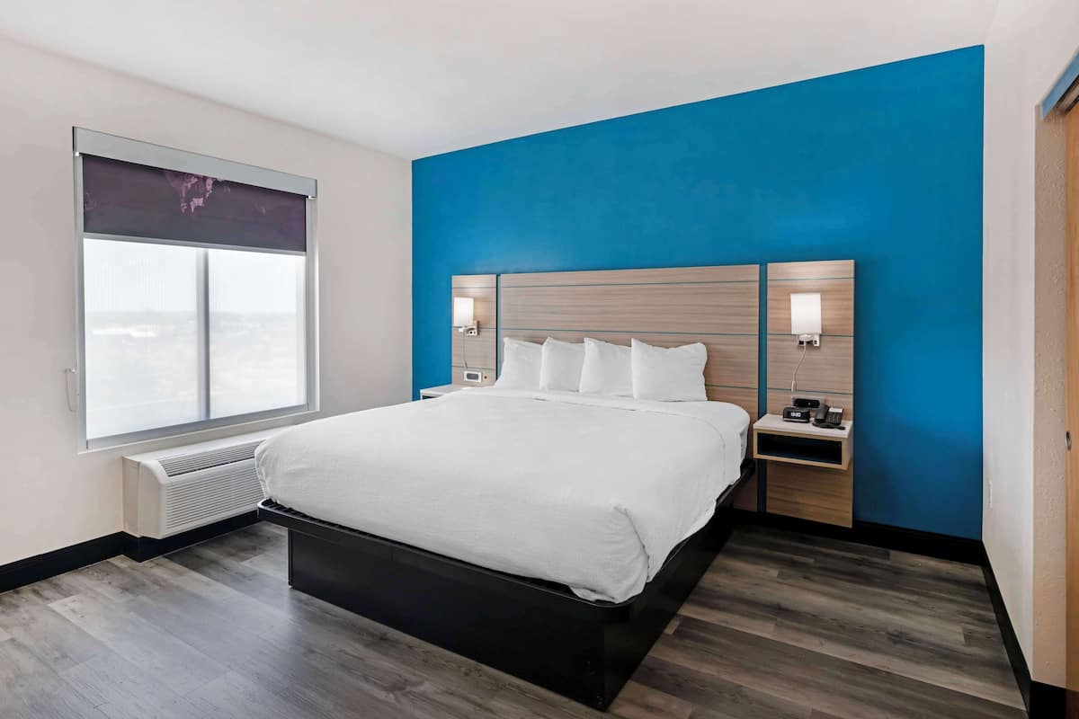 Ein modernes Hotelzimmer mit einem großen Bett, einem Nachttisch, einer Wandlampe und einem Fenster mit Blick.