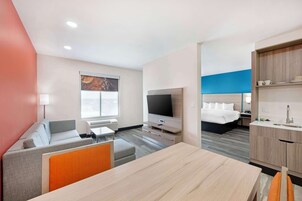 Una habitación de hotel moderna con sofá, mesa de comedor, televisor, cama y kitchenette.