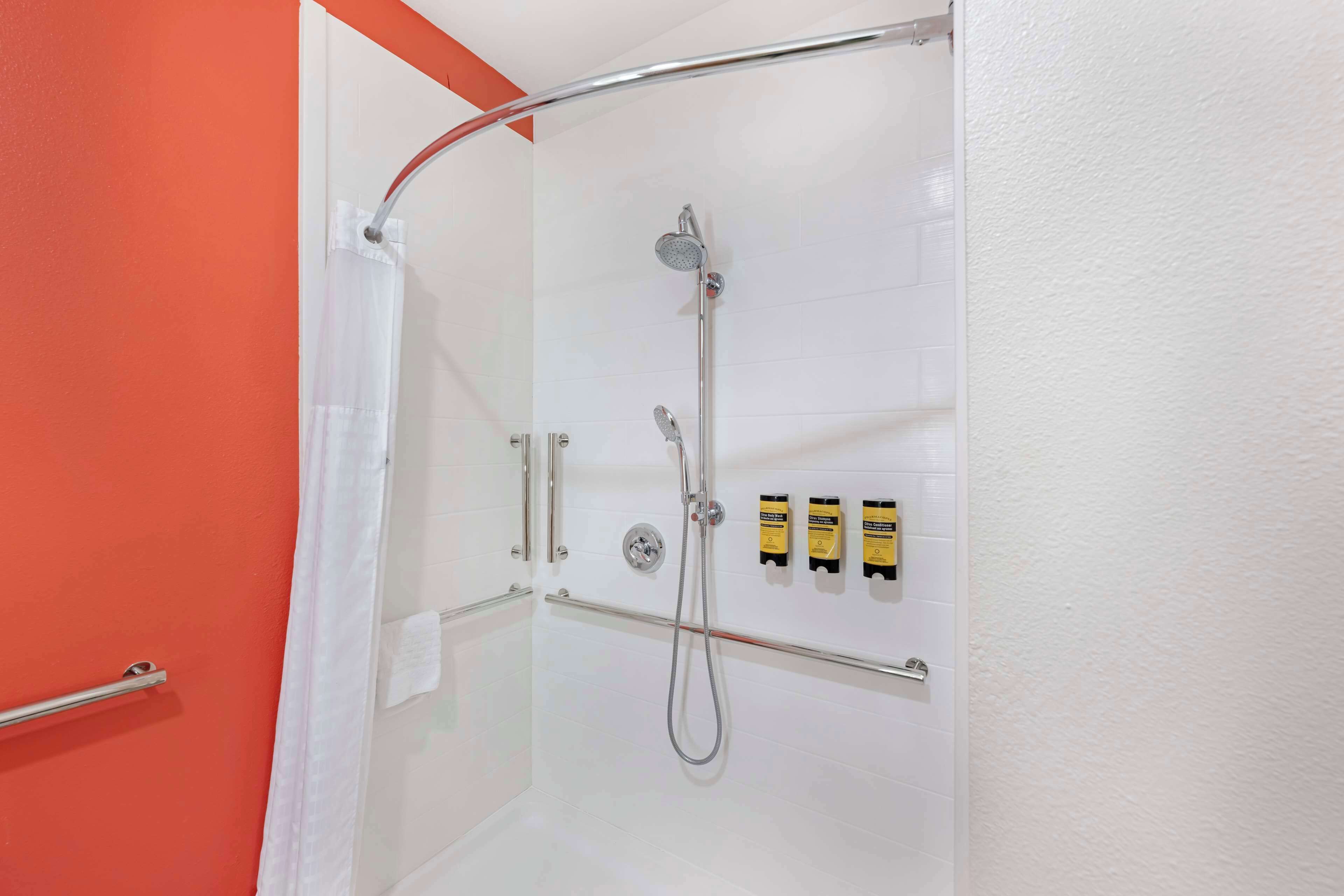 A shower area with a glass door, a handrail, and three toiletries on the wall.