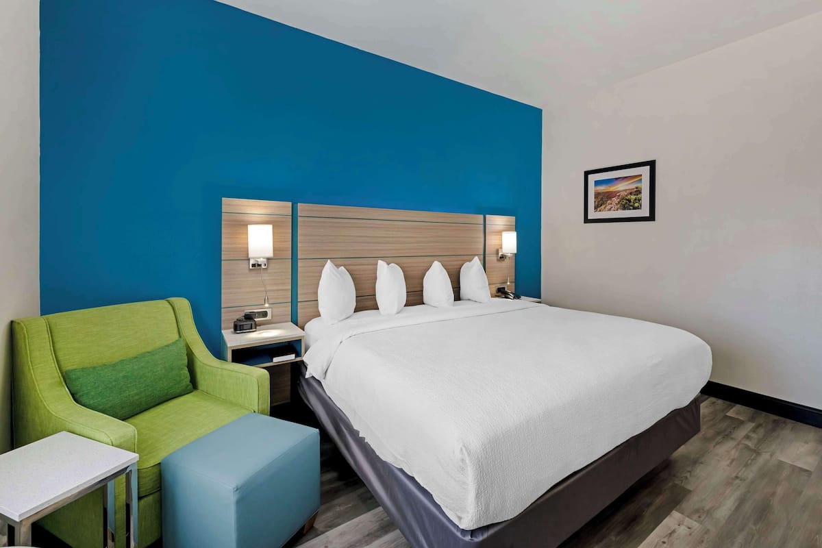 Ein Hotelzimmer mit einem großen Bett, einem grünen Sessel, einem kleinen Tisch und einem Nachttisch mit einer Lampe.