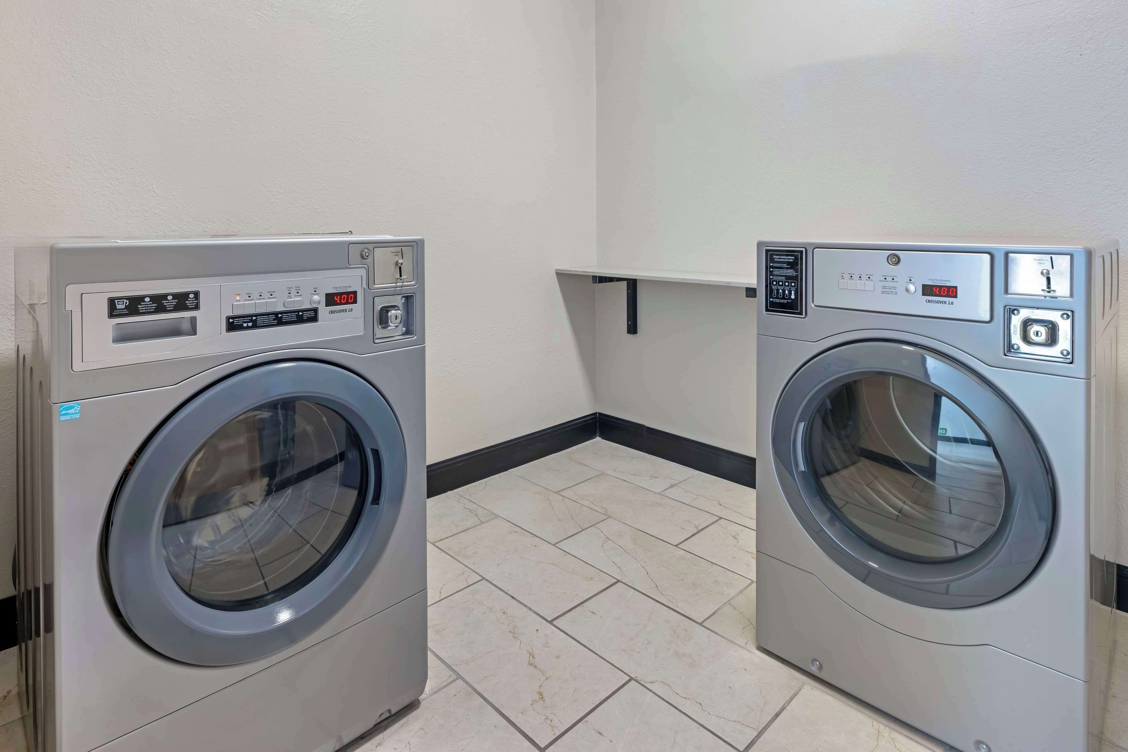 Two front-loading washing machines in a laundry room with tiled flooring and a white wall.
