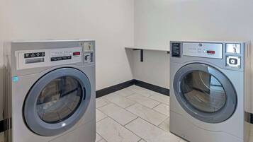 Two front-loading washing machines in a laundry room with tiled flooring and a white wall.