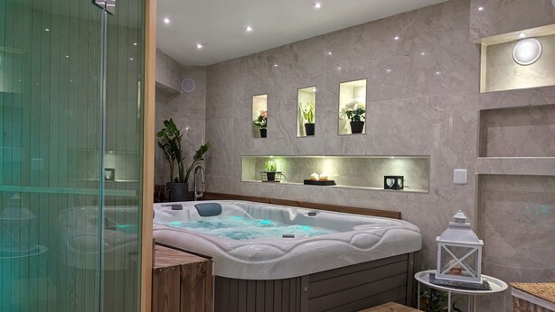 Een moderne badkamer met een groot bad, houten bankjes en potplanten.