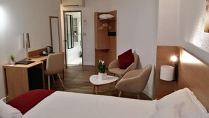 Een hotelkamer met een bed, een bureau, een stoel, een klein tafeltje en een bedlampje.
