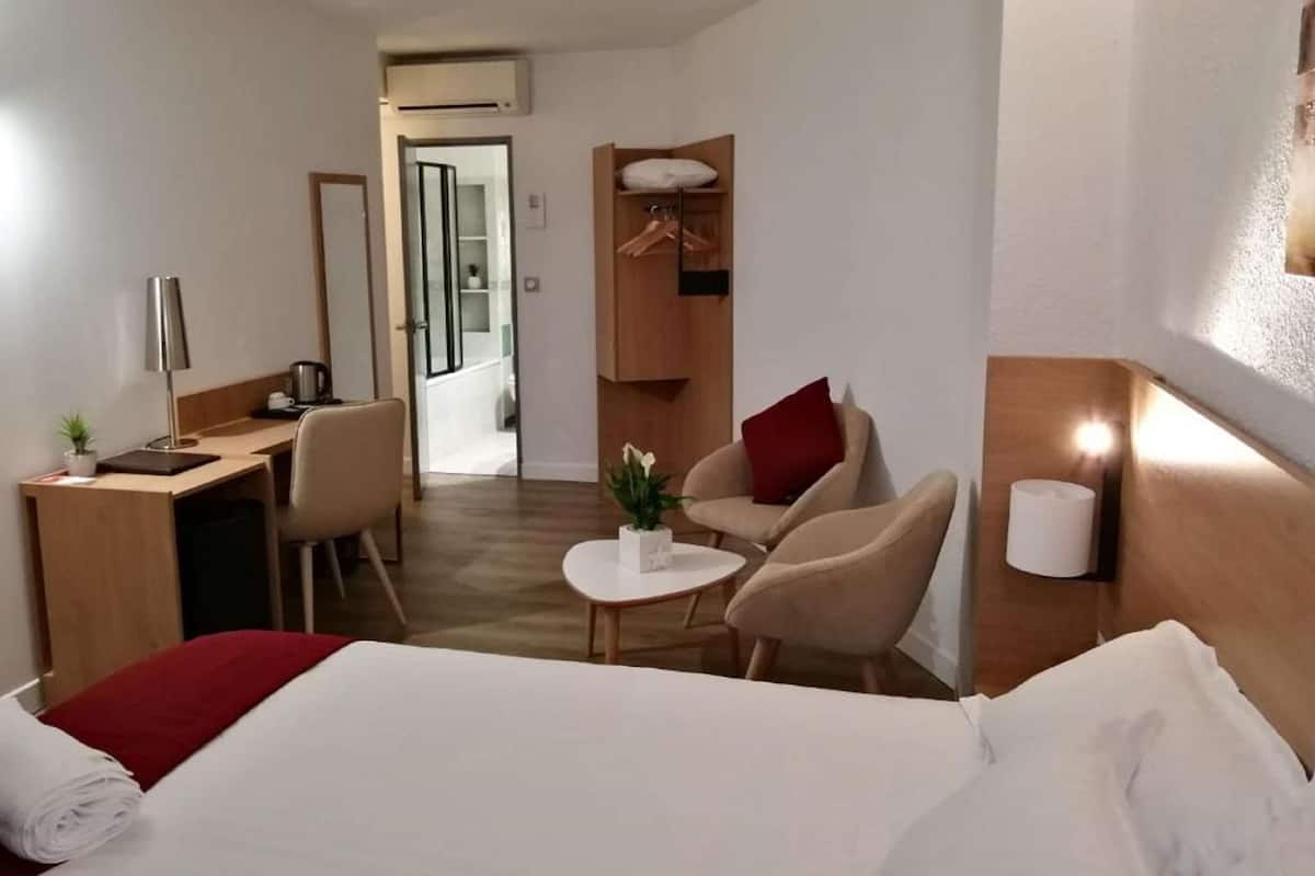 Une chambre d’hôtel comprenant un lit, un bureau, une chaise, une petite table et une lampe de chevet.