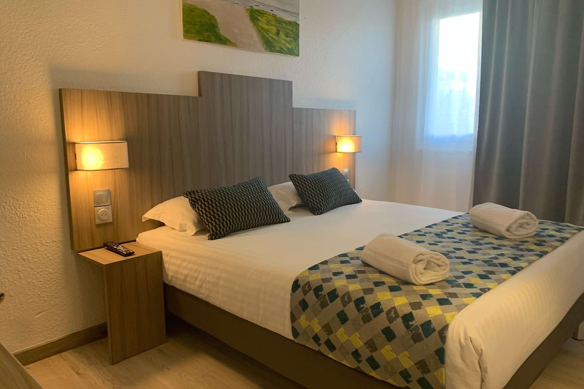 Une chambre d’hôtel avec un grand lit, deux lampes de chevet, une table de nuit, un tableau au mur et une fenêtre avec des rideaux.
