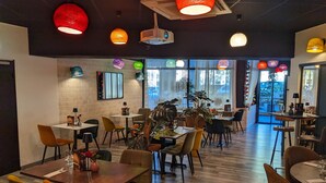 Een restaurantinterieur met meerdere tafels en stoelen, een bakstenen muur en grote ramen.