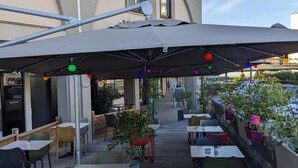 Een buitenzitgedeelte met tafels en stoelen, een overdeeld deel met parasols, en een gebouw met een bord waarop 