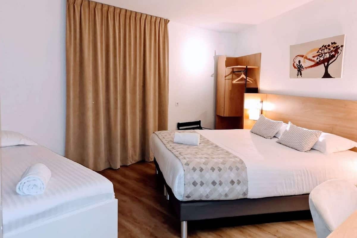Une chambre d’hôtel avec un lit, une table de chevet, une chaise, une armoire et un tableau au mur.
