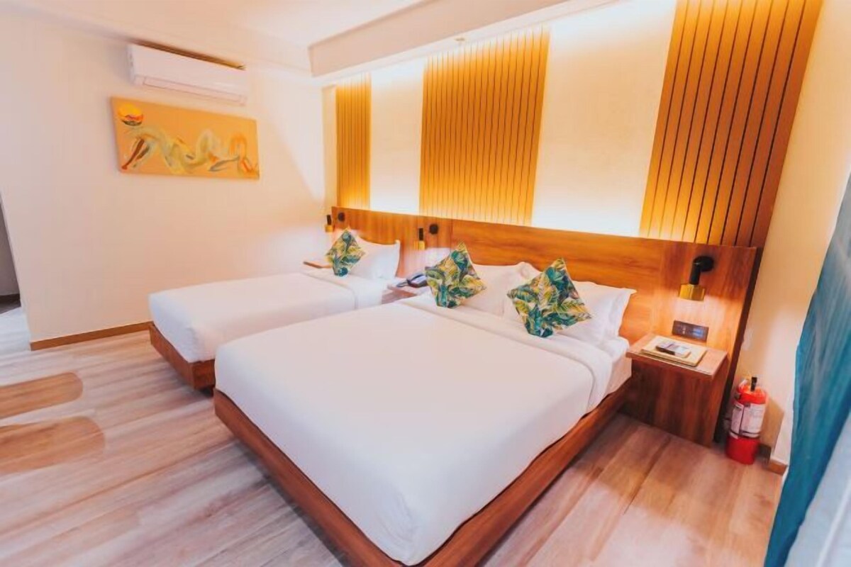 A hotel room with two beds, a wooden headboard, a bedside table with a lamp, and a wall-mounted air conditioner.