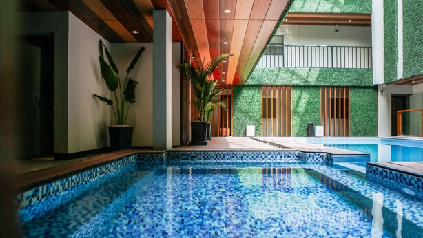 Une piscine intérieure moderne, avec un sol carrelé en mosaïque, des poutres en bois au plafond et des plantes en pot.