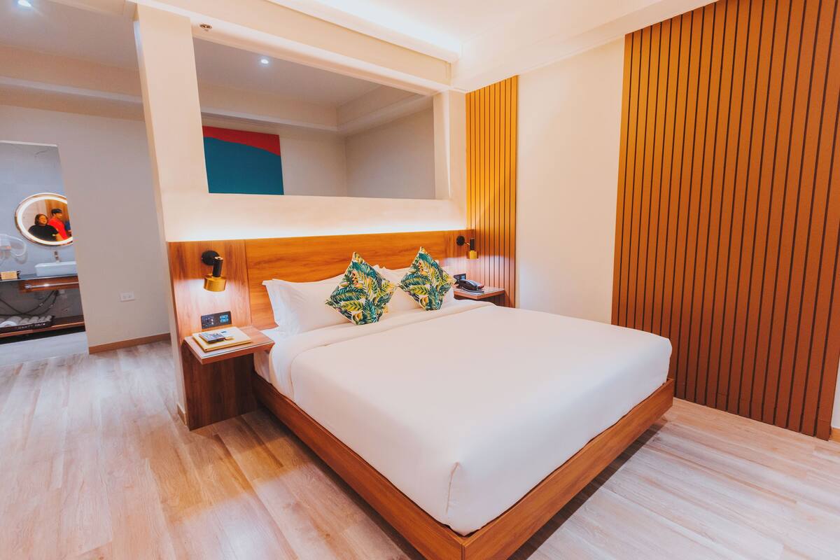 Ein modernes Hotelzimmer mit einem großen Bett, einem Holzkopfteil und einem integrierten Schminktisch mit Spiegel.