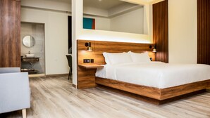 Une chambre moderne avec une tête de lit en bois, une table de chevet, une chaise et une étagère intégrée dotée d’un miroir et d’un lavabo.