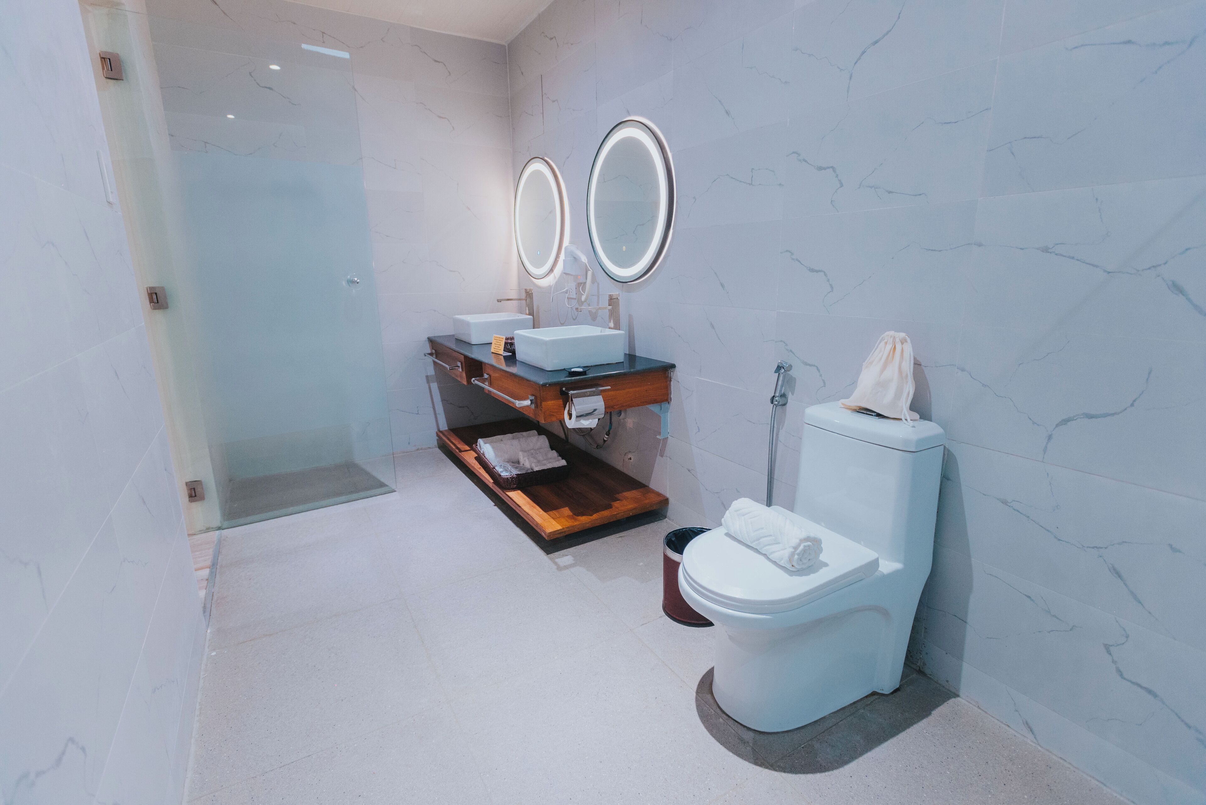 A modern bathroom with a glass shower enclosure, two round mirrors, a wooden vanity, and a white toilet.