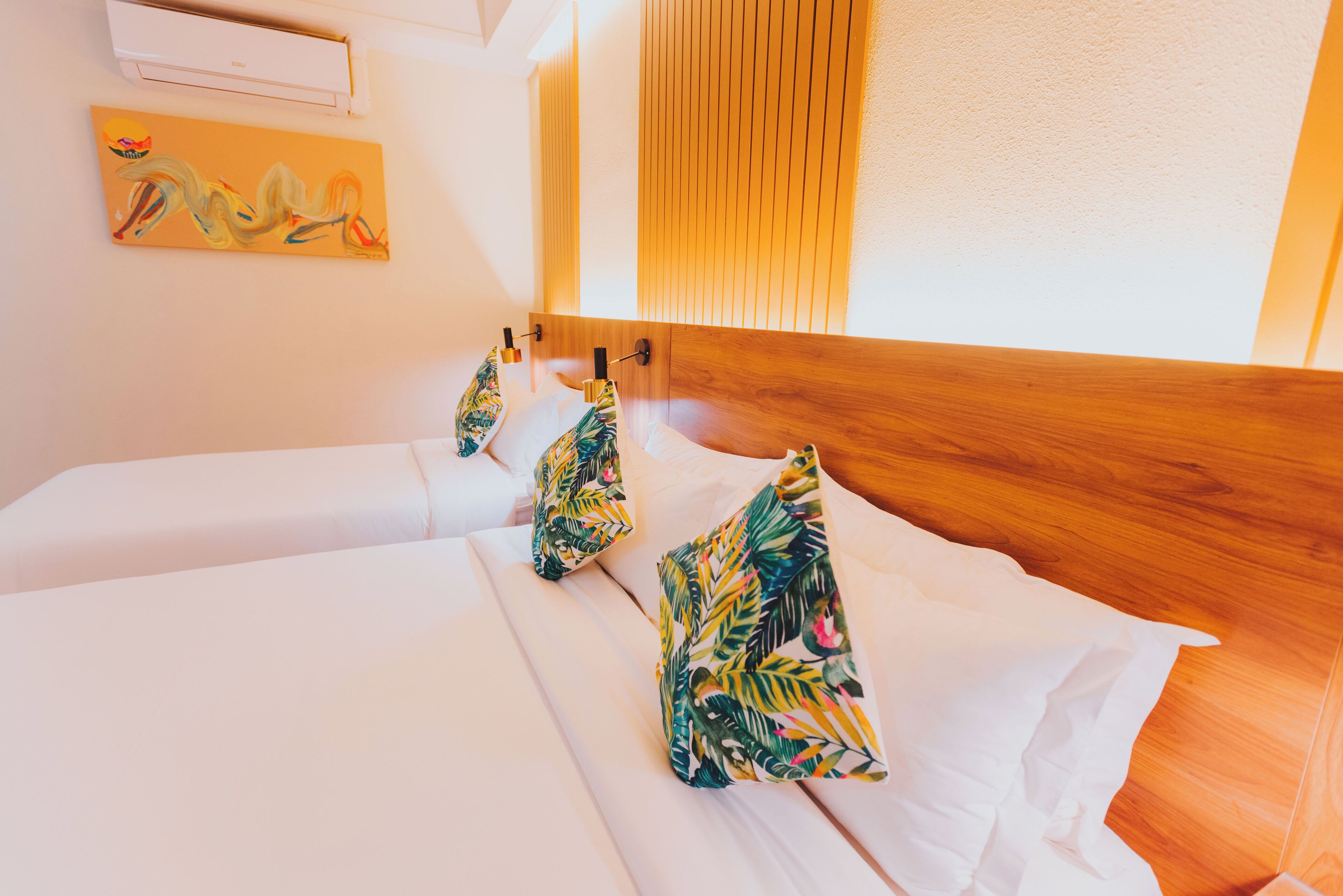 Ein Hotelzimmer mit zwei Betten, einem Holzkopfteil, einer Wand-Klimaanlage und einem Gemälde.