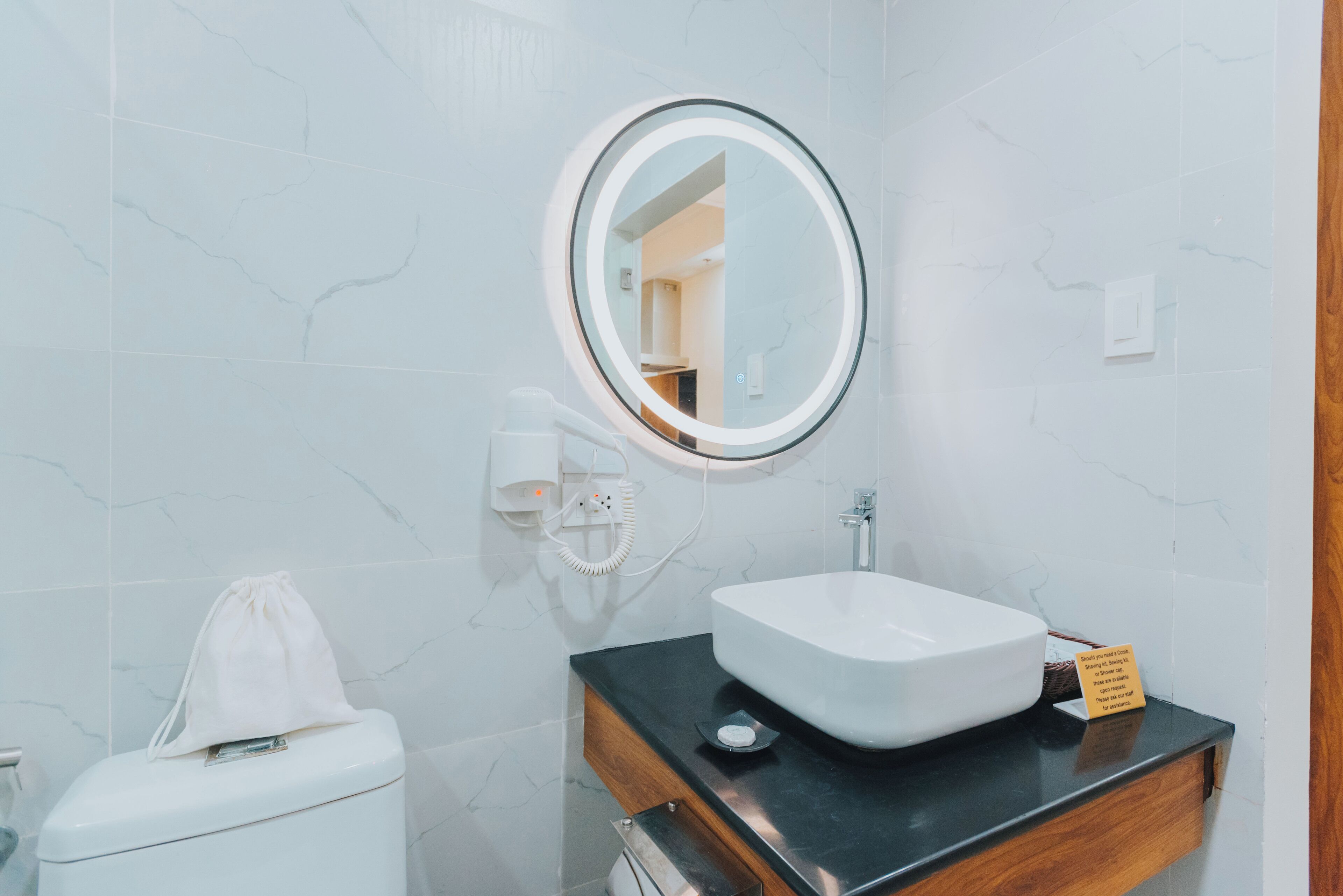 Un baño con inodoro blanco, espejo redondo, lavabo blanco y tocador de madera.