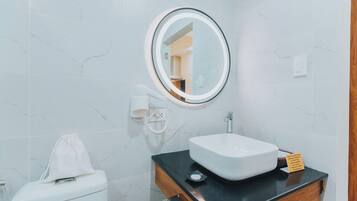 A bathroom with a white toilet, a round mirror, a white sink, and a wooden vanity.
