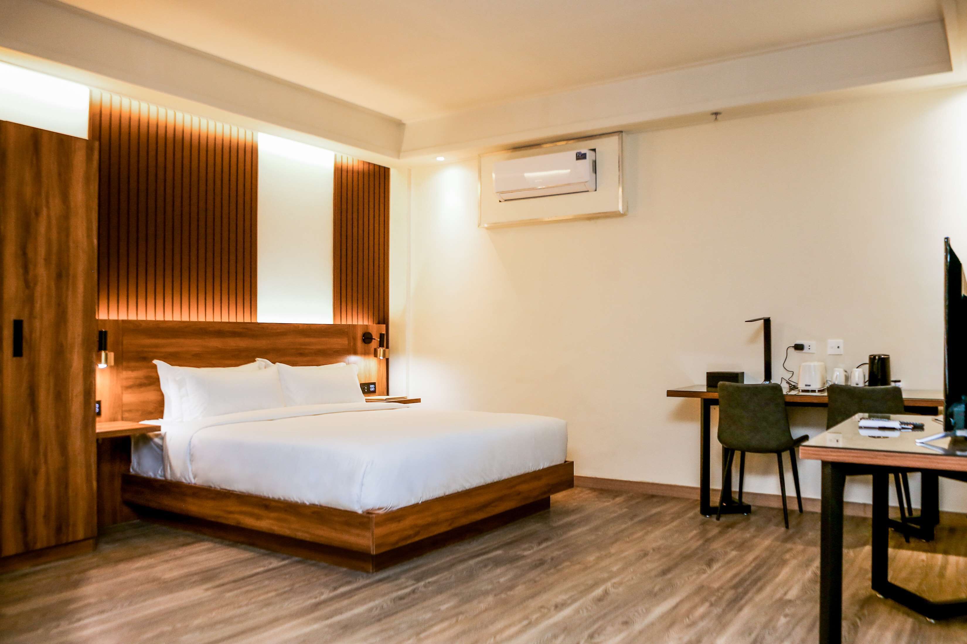 Una habitación de hotel moderna con una cama de madera, un escritorio con una silla y un equipo de aire acondicionado en la pared.
