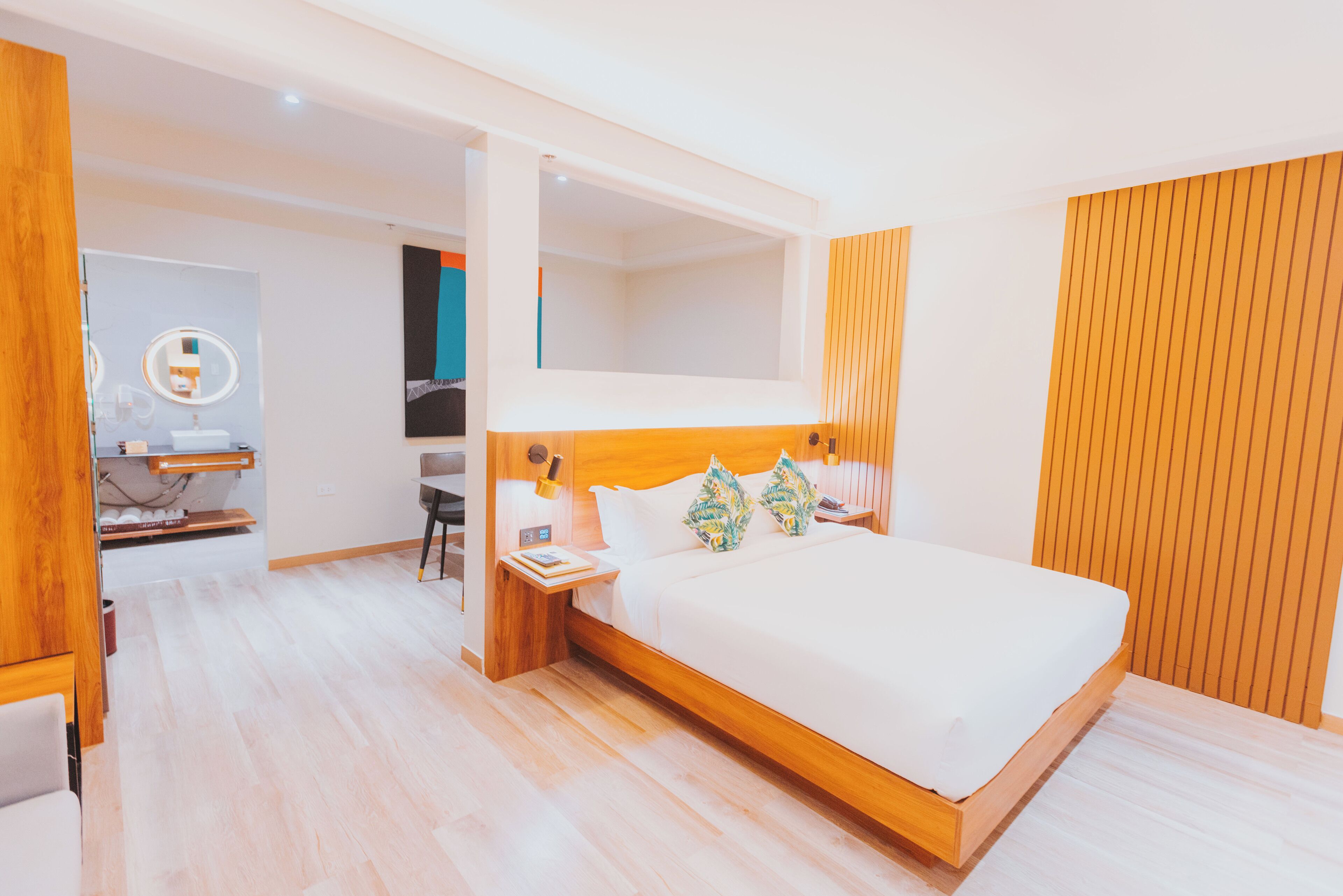 A modern hotel room with a large bed, wooden headboard, and a desk with a chair.