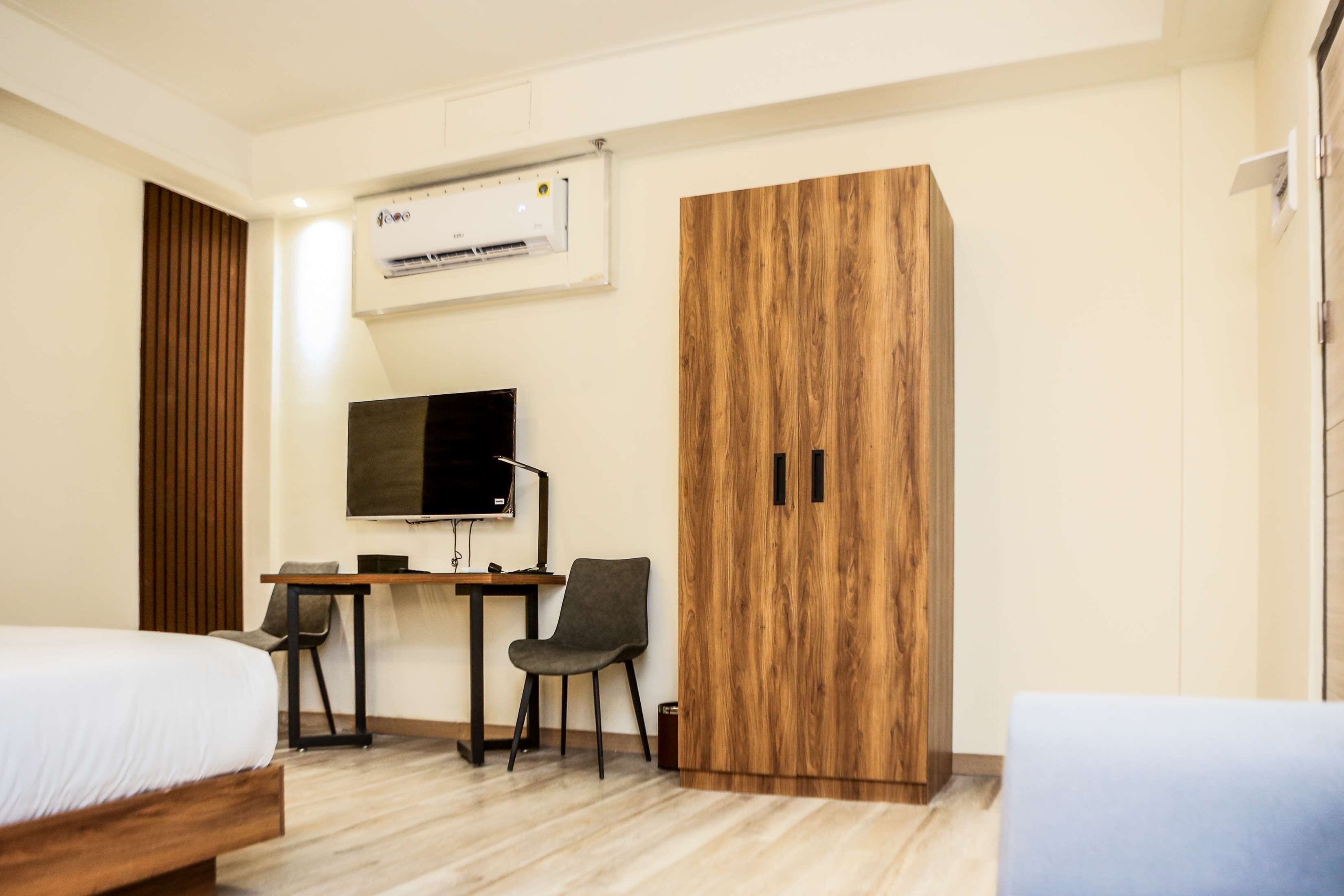 A hotel room with a bed, a desk with a chair, a TV, and a wardrobe.