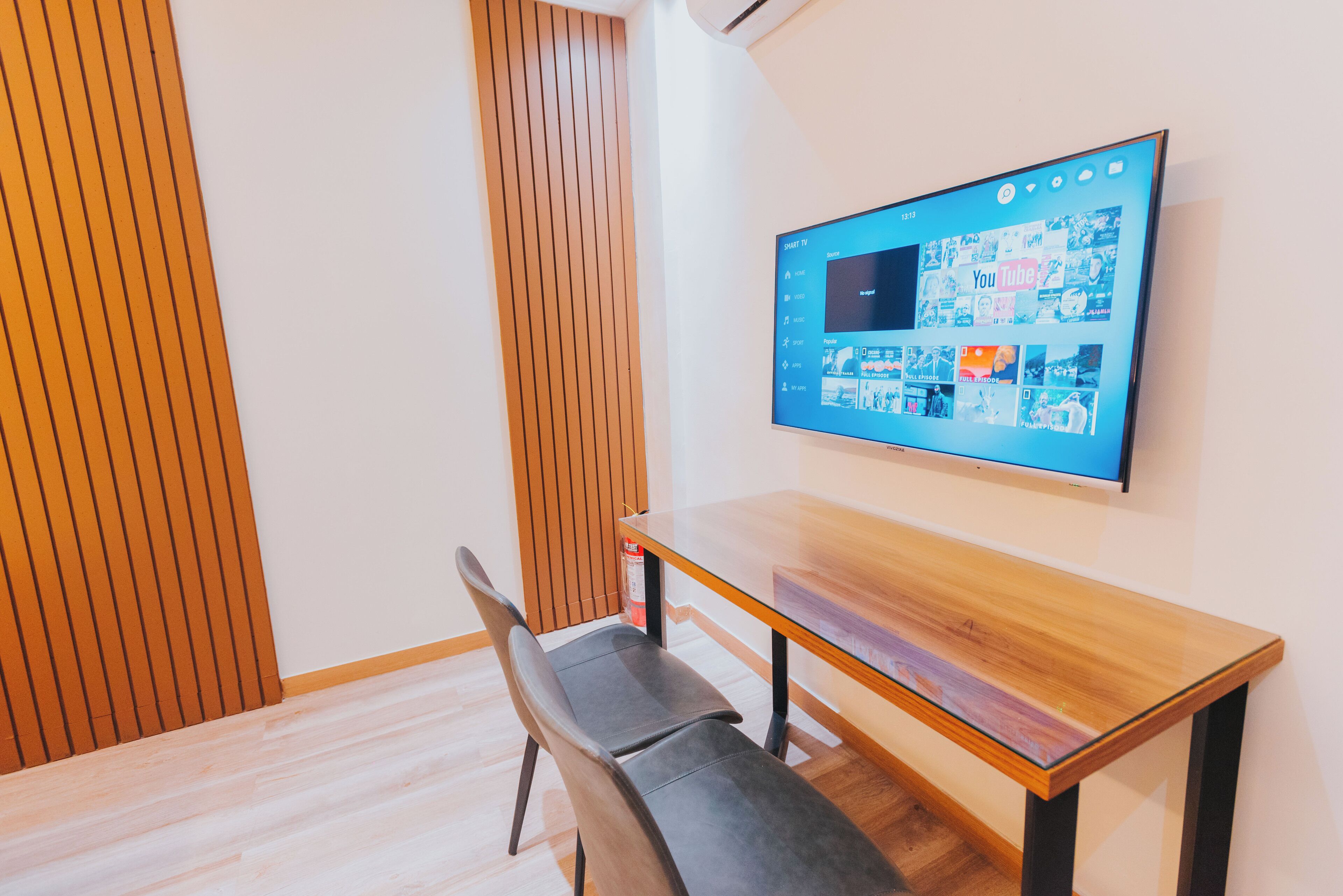 A modern room with a wooden table, a grey chair, and a mounted flat-screen TV displaying a YouTube channel.