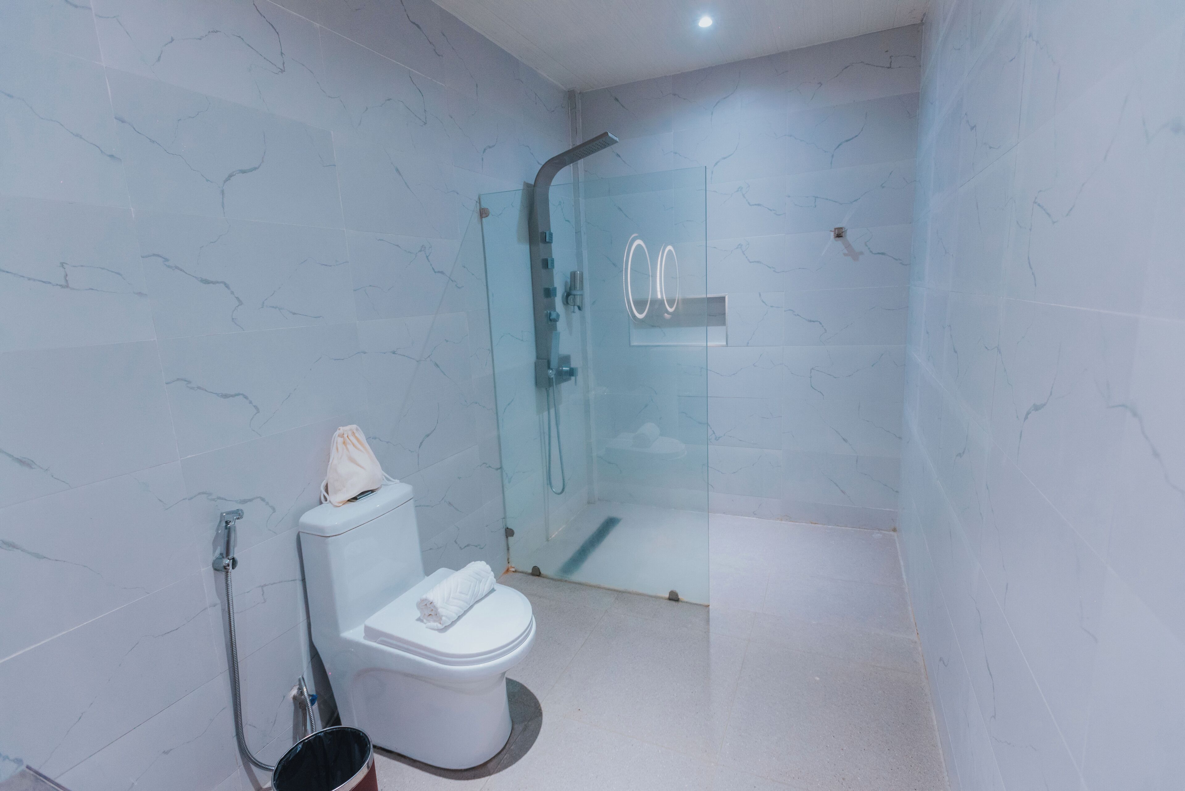 Un baño moderno con ducha envuelta en vidrio, inodoro con toalla y puerta de cristal.