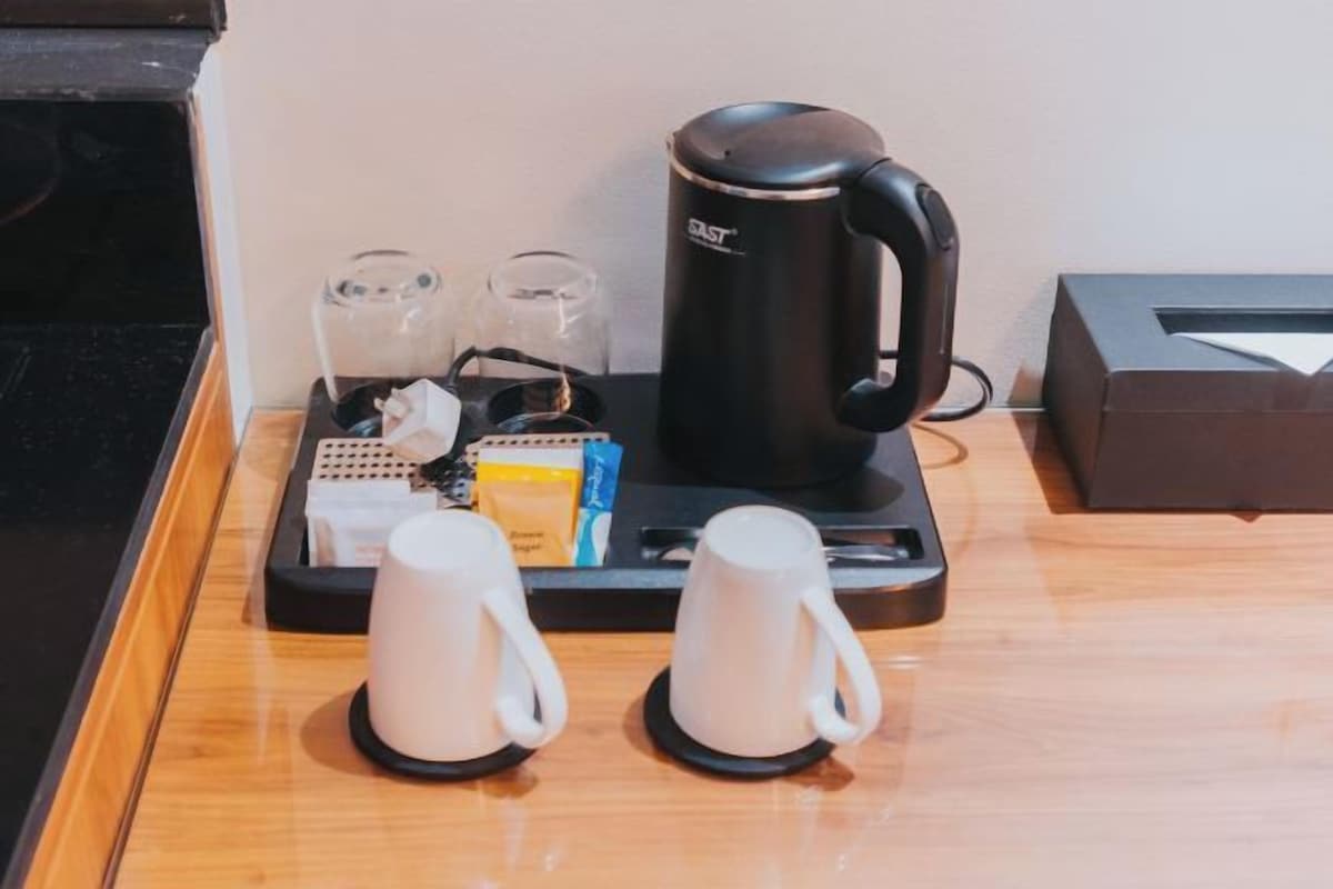 Una estación de café con una cafetera negra, dos tazas blancas y una bandeja con cápsulas de café e sobres de azúcar.