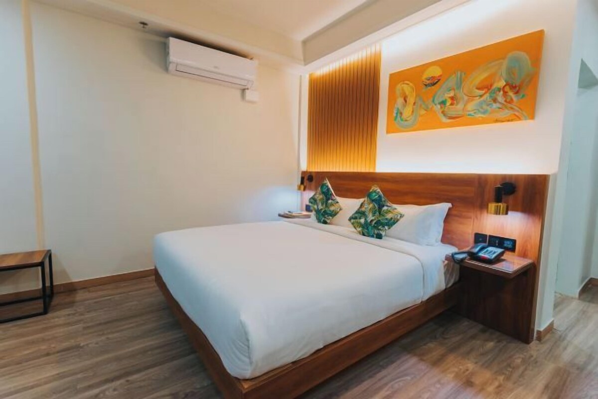 A neatly arranged hotel room with a large bed, wooden headboard, and a wall-mounted air conditioner.