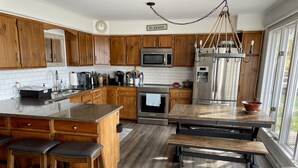 Une cuisine moderne avec des meubles en bois, des appareils en acier inoxydable, un grand îlot central doté de tabourets et une vue sur l’extérieur.