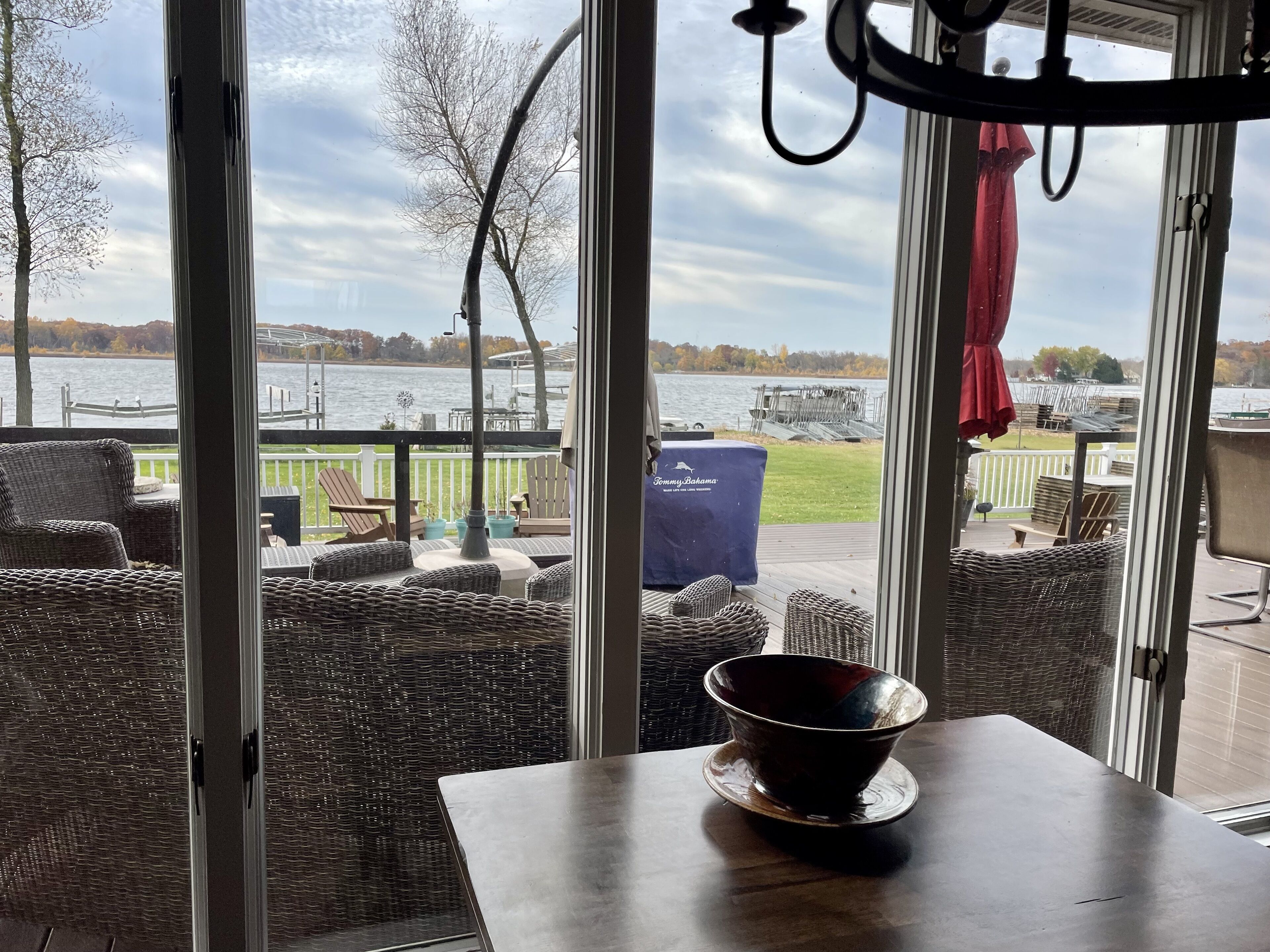 A room with a view of a lake, wicker furniture, and a table with a bowl.