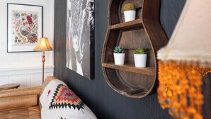 A cozy living room with a dark wall, a wooden shelf with plants, a framed artwork, and a lamp. - The Downtown Hive by Revelstoke Vacations (Revelstoke)